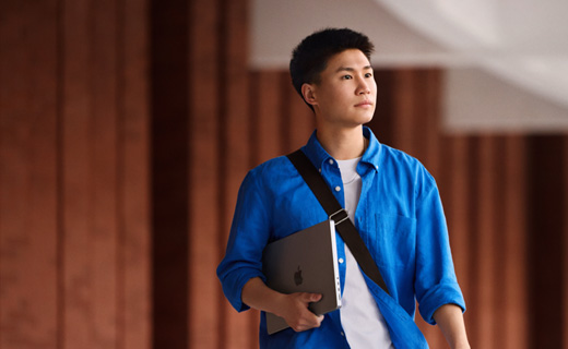 照片展示一个男生手捧 MacBook Pro，在校园里行走。