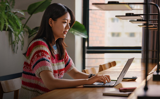照片展示大学图书馆里，一位女生正坐在书桌前使用 MacBook Pro。