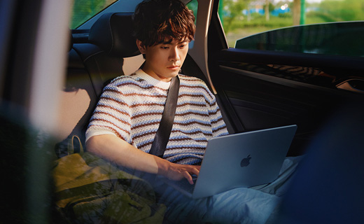 照片展示一个男生坐在轿车后排用着 MacBook Air。
