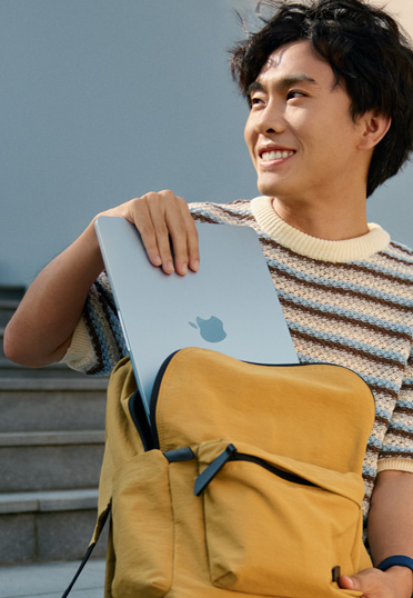 一名学生坐在外面。他从书包里拿出一台封闭的 MacBook。