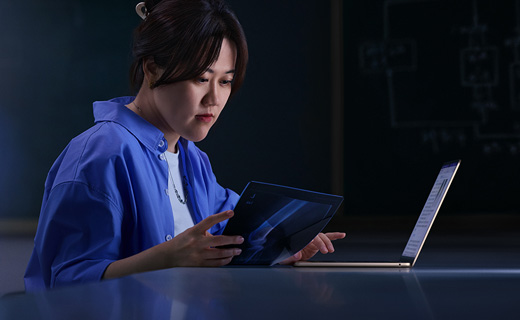 照片展示一位女生坐在书桌前用着 MacBook Air，同时一手拿着一张 X 光片。